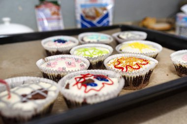 Beyaz kağıda sarılı çikolatalı çörekler ve renkli süslemelerle kaplanmış beyaz kremayla fırında pişmiş, pişmiş kağıt üzerinde yatıyorlar..