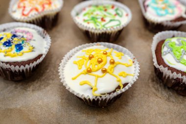 Beyaz kağıda sarılı çikolatalı çörekler ve renkli süslemelerle kaplanmış beyaz kremayla fırında pişmiş, pişmiş kağıt üzerinde yatıyorlar..