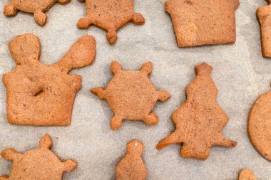 Çeşitli şekillerde fırınlanmış zencefilli kurabiyeler dekorasyonsuz, kağıt üzerinde uzanmış, üst görünüm.