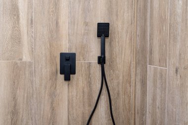 Siyah, mat el duşu fayanslı bir duvara monte edilmiş, ahşabı taklit ediyor..