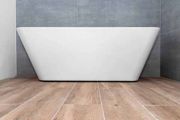 A modern, free-standing wall-mounted bathtub, without a tap, standing in a bathroom lined with ceramic tiles.