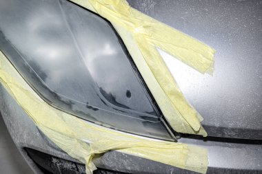 The headlight is covered with abrasive paste and secured with a protective tape, prepared for polishing. clipart