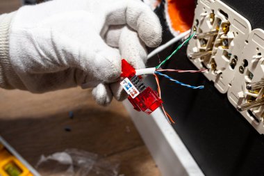 Beyaz eldivenli bir elektrikçi odadaki bilgisayar soketine RJ45 modülü için ağ kablosu kuruyor..