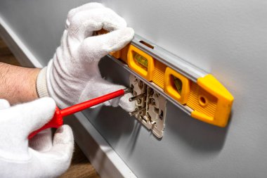 Bir elektrikçi çift topraklı bir elektrik prizini odanın duvarına vidalamak için kırmızı bir tornavida kullanır ve bunu dengelemek için ruh seviyesini kullanır..