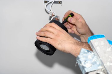 Bir elektrikçi, bir tornavida kullanarak, modern LED aydınlatmayı bir tüp şeklinde monte eder, Matt siyah boya ile boyanmış, bir kablo kıskacı ile.