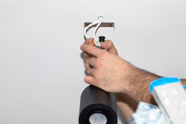 Bir elektrikçi, bir tornavida kullanarak, modern LED aydınlatmayı bir tüp şeklinde monte eder, Matt siyah boya ile boyanmış, bir kablo kıskacı ile.