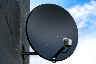 Black satellite dish mounted to the facade of the house, which is covered with black styrofoam.