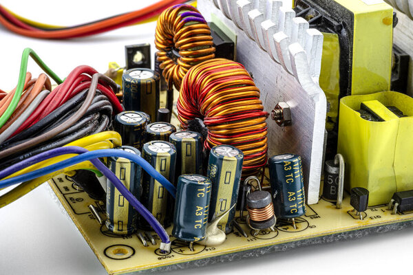 Индукционная катушка, тороидальная катушка на кольце с видимой медной спиралью и конденсаторами, установленная на печатной плате в блоке питания компьютера.