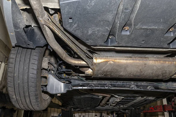 The exhaust system in the car seen from below, visible end silencer and wheel, the car is on the lift in the car workshop