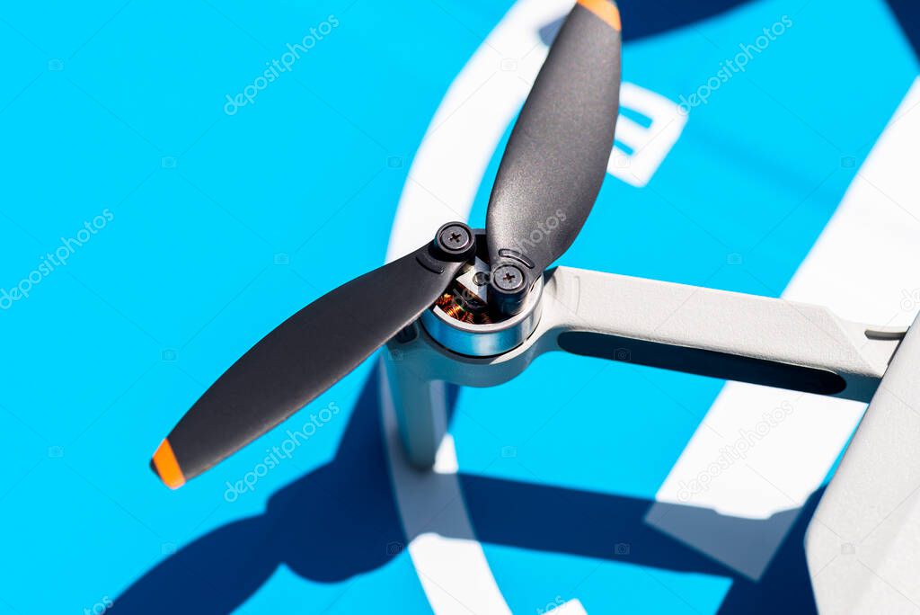 A close-up shot of the complex propellers and brushless motor of a drone against the backdrop of a blue landing pad.