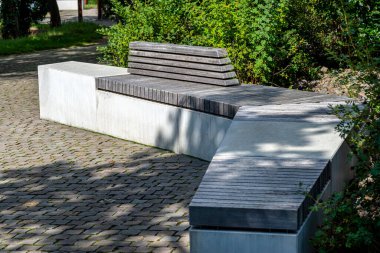 Kaldırımın kenarındaki parkta duran tahta koltuklu beton bir bank..