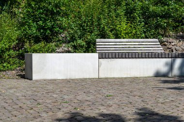 Kaldırımın kenarındaki parkta duran tahta koltuklu beton bir bank..