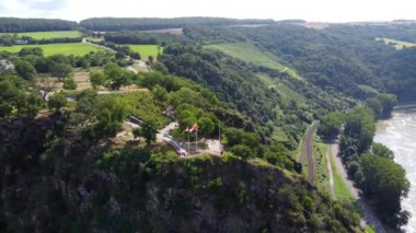 Video from a drone moving away from a cliff on the Rhine in Germany, visible road on both sides of the river.