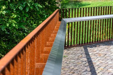 Nehir vadisinin kıyısındaki paslı metal çitler, görünür çimenler..