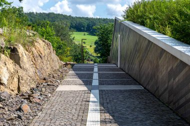 Kayalarla binanın duvarları arasında uzanan kaldırım taşlarından oluşan bir sokak. Ağaçlı bir tarla..