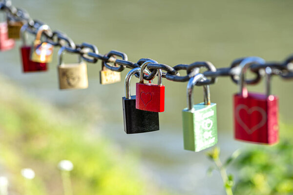 Red padlock suspended on a chain engraved with one heart.