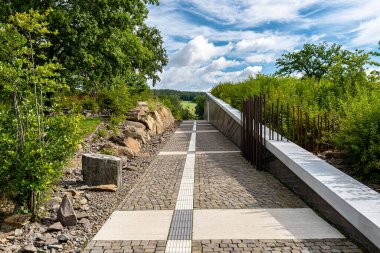 Kayalarla binanın duvarları arasında uzanan kaldırım taşlarından oluşan bir sokak. Ağaçlı bir tarla..