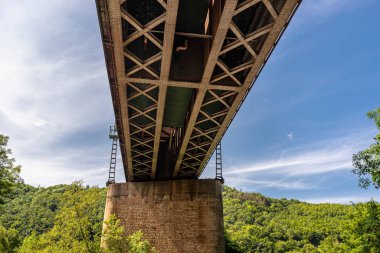 Demiryolu köprüsünün çelik kafes yapısı aşağıdan mavi gökyüzüne bakıyordu..