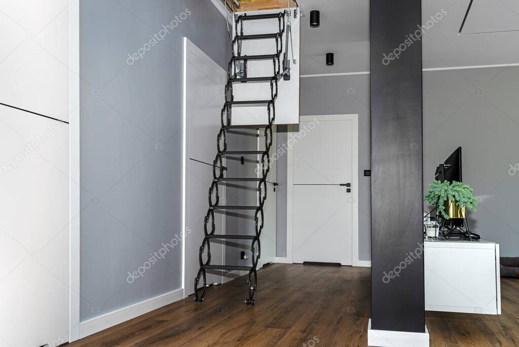 Metal stairs hidden in the ceiling to the attic with an opening hatch and folding stairs in the corridor, modern look.