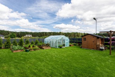 Evin arkasındaki çimlerin üzerinde duran folyodan yapılmış arka bahçe serası..