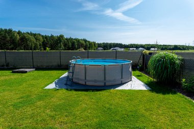 Çapı 3.96 metre olan büyük bir genişleme havuzu bahçedeki çimlerin üzerinde plastik bir yaprak üzerine yerleştirilir..