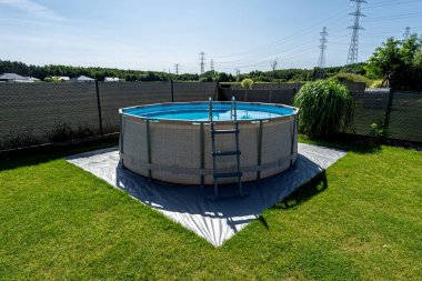 Çapı 3.96 metre olan büyük bir genişleme havuzu bahçedeki çimlerin üzerinde plastik bir yaprak üzerine yerleştirilir..