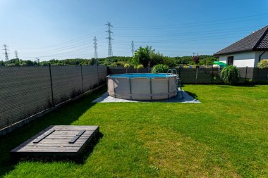 Çapı 3.96 metre olan büyük bir genişleme havuzu bahçedeki çimlerin üzerinde plastik bir yaprak üzerine yerleştirilir..