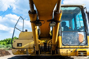 Mavi gökyüzünün altındaki bir inşaat alanında çalışan sarı hidrolik kazıcı