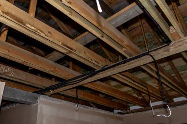 Evin yenilenmesi sırasında açıkta olan ahşap çatı kirişleri boyunca elektrik kabloları ve kanallar çalışıyor.