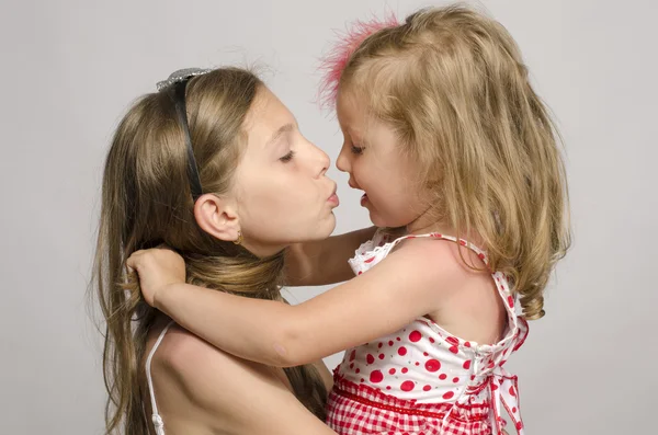 Chica joven sosteniendo en sus brazos y besándose y divirtiéndose con su hermana pequeña. Niños jugando y riendo —  Fotos de Stock