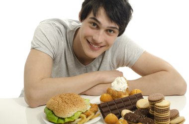 Young man holding in front lots of cookies and a big hamburger. Choosing between chocolate, cupcakes, biscuits and a burger. Trying to get fat eating fast food and lots of sugar clipart