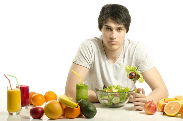 Uomo con un tavolo pieno di cibo biologico, succhi di frutta e frullato. Giovane allegro che mangia insalata sana, frutta e beve frullato biologico. Isolato su bianco — Foto Stock