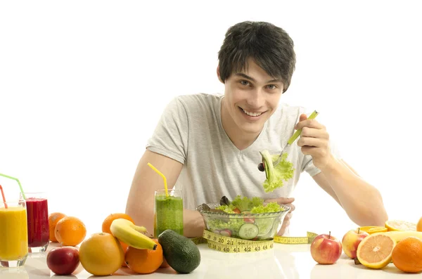Mann mit Tisch voller Biolebensmittel, Säften und Smoothie. fröhlicher junger Mann isst gesunden Salat, Obst und trinkt Bio-Smoothie. isoliert auf weiß — Stockfoto