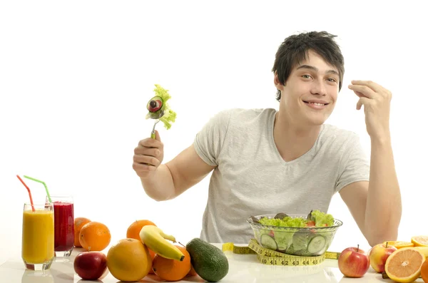 Homem tendo uma mesa cheia de alimentos orgânicos, sucos e smoothie. Jovem alegre comendo salada saudável, frutas e bebendo smoothie orgânico. Isolado em branco — Fotografia de Stock