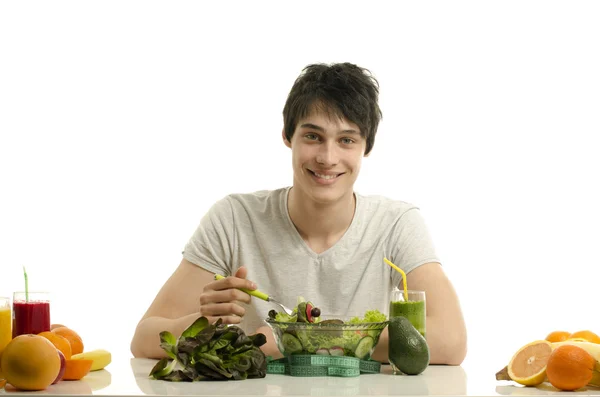 Man har ett bord fullt av ekologiska livsmedel, juice och smoothie. glad ung man äta hälsosam sallad, frukt och dricka ekologisk smoothie. isolerad på vit — Stockfoto