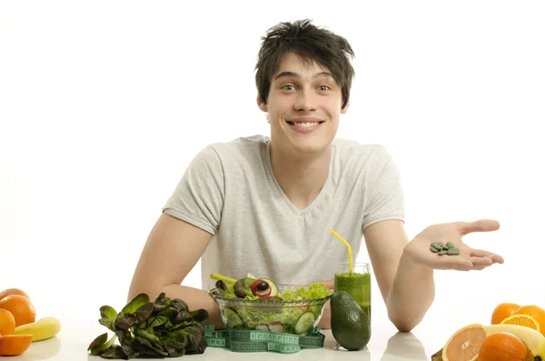 Muž, volba mezi jíst zdravé ekologické potraviny a léky. šťastný muž s stůl plný biopotravin, džusy a koktejl. jíst zelené potraviny a užívání pilulky spirulina — Stock fotografie
