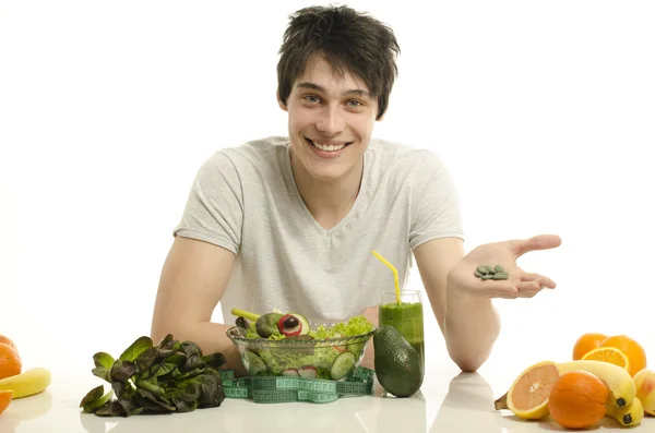 Homme qui choisit entre manger des aliments biologiques sains et des pilules. Heureux homme ayant une table pleine d'aliments biologiques, jus et smoothie. Manger des aliments verts et prendre des pilules de spiruline — Photo