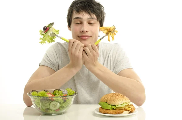 Jonge man houden aan de voorkant een kom van salade en een grote hamburger. kiezen tussen goed gezond voedsel en slechte ongezond voedsel. Natuurvoeding versus fastfood — Stockfoto