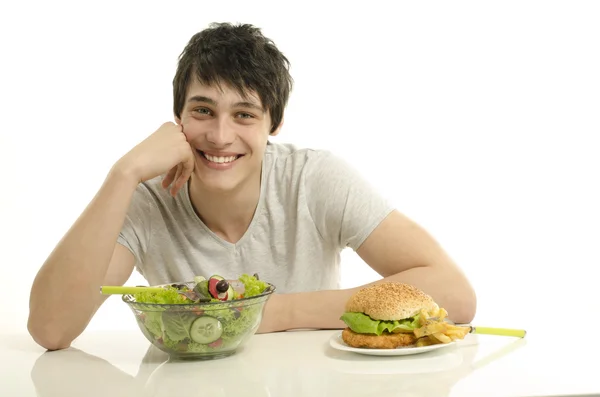 Genç adam, önünde büyük bir hamburger ve salata bir kase tutarak. iyi sağlıklı yemek ve kötü sağlıksız yemekler arasında seçim yapma. fast food karşı organik gıda — Stok fotoğraf