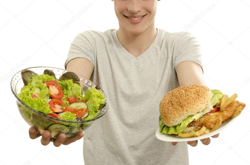 Man offering you a salad and a hamburger. Young man holding in front a bowl of salad and a big burger. Choosing between good healthy food and bad unhealthy food. Fast food versus organic