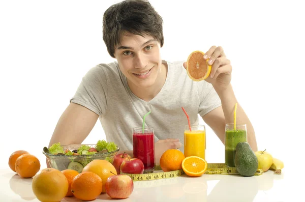 Mann mit Tisch voller Biolebensmittel, Säften und Smoothie. fröhlicher junger Mann isst gesunden Salat, Obst und trinkt einen gelben Smoothie. isoliert auf weiß — Stockfoto