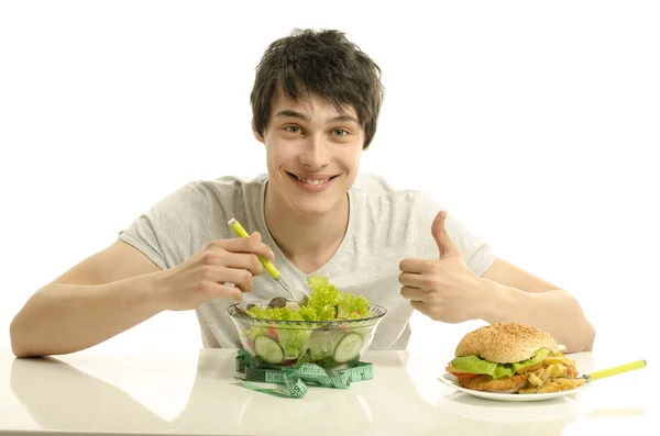 Genç adam, önünde büyük bir hamburger ve salata bir kase tutarak. iyi sağlıklı yemek ve kötü sağlıksız yemekler arasında seçim yapma. fast food karşı organik gıda — Stok fotoğraf