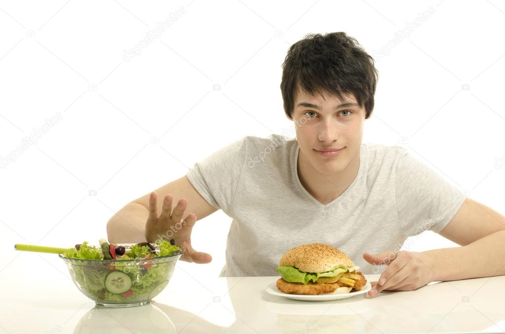 Young man holding in front a bowl of salad and a big hamburger. Choosing between good healthy food and bad unhealthy food. Organic food versus fast food