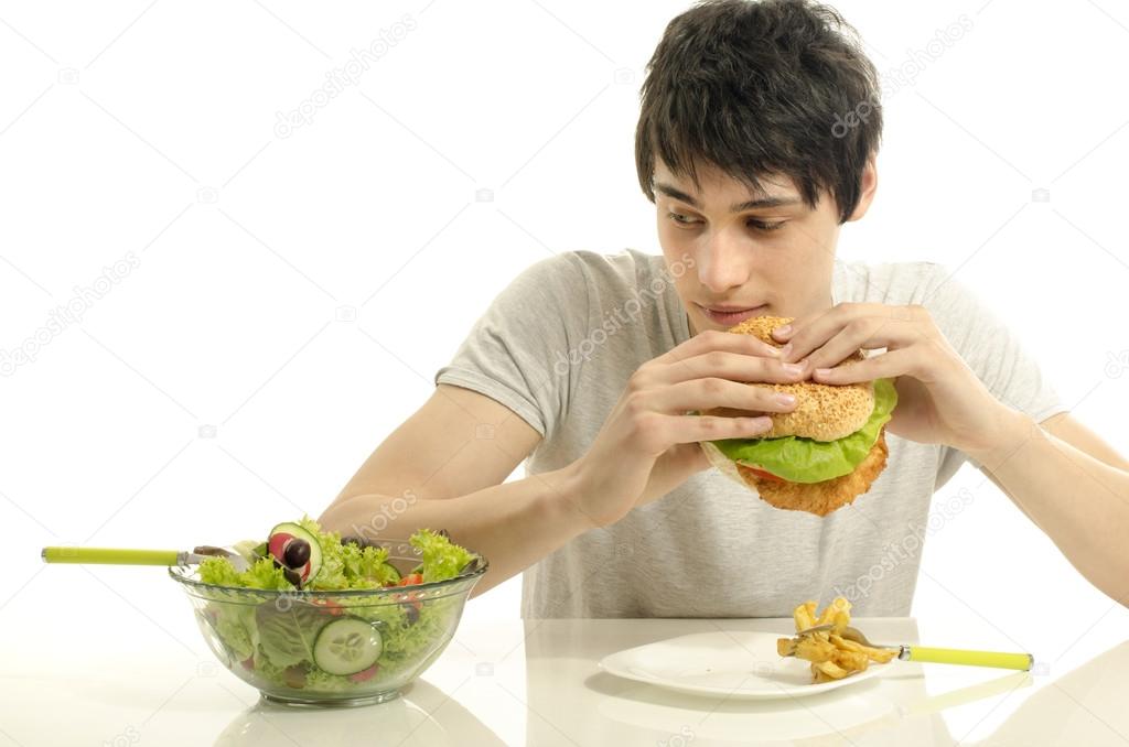 Young man holding in front a bowl of salad and a big hamburger. Choosing between good healthy food and bad unhealthy food. Organic food versus fast food