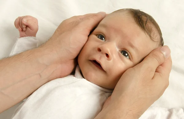 Um lindo recém-nascido inocente a olhar para o pai. Menino adorável relaxando em lençóis brancos depois de um banho, as mãos do pai segurando seu recém-nascido com amor — Fotografia de Stock