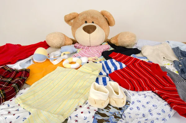 Beer speelgoed op een bed met verschillende kleurrijke pasgeboren kleding.Kleurrijke garderobe van pasgeborenen, kinderen, baby 's vol van alle kleding, schoenen, accessoires en speelgoed — Stockfoto