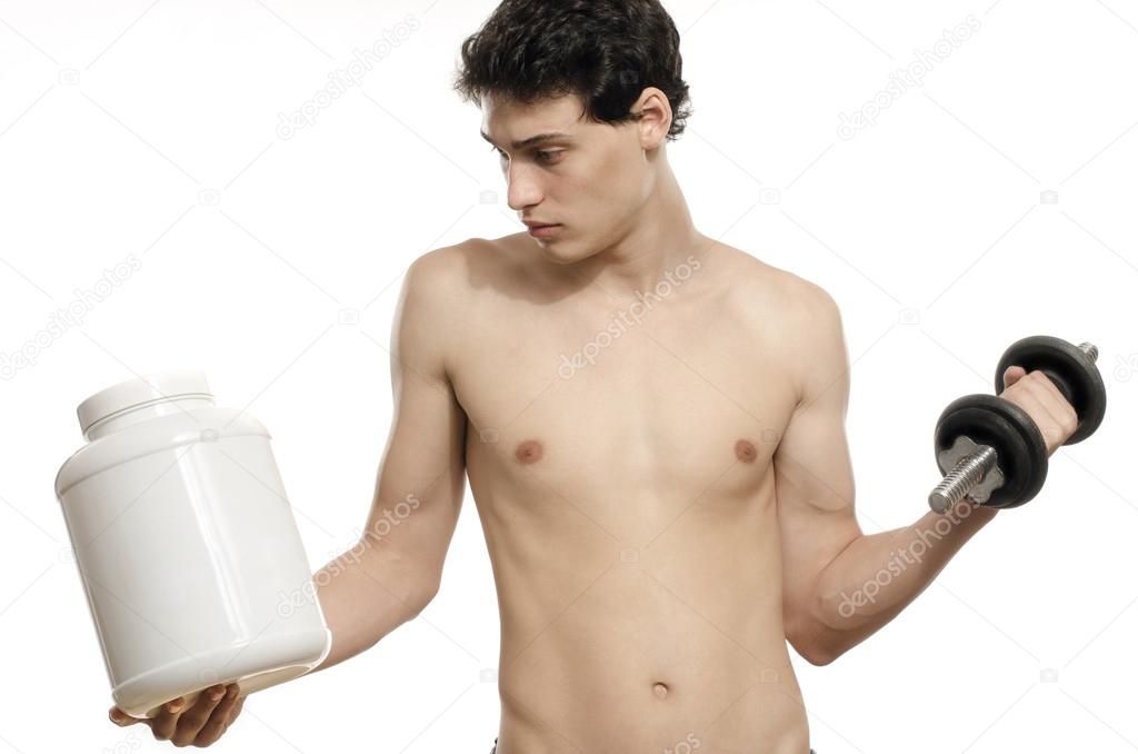 Skinny man traininghis biceps muscle and taking a protein shake. Beautiful teenager lifting a dumbbell.Anorexic young man training to become stronger and using steroids