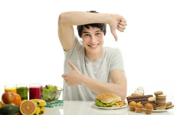 Homem escolhendo entre frutas, smoothie e alimentos orgânicos saudáveis contra doces, açúcar, lotes de doces e um grande hambúrguer, fast food — Fotografia de Stock