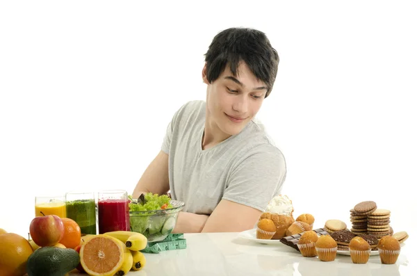 Man choosing between fruits, smoothie and organic healthy food against sweets, sugar, lots of candies and a big hamburger, fast food — Stock Photo, Image