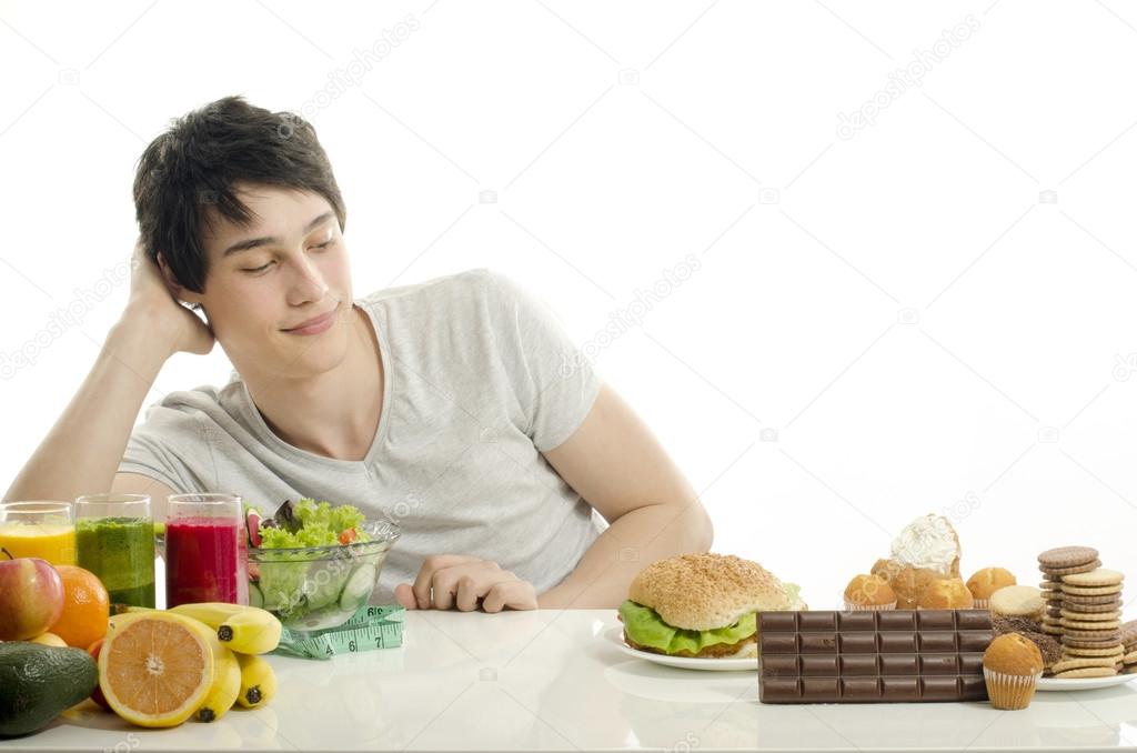 Man choosing between fruits, smoothie and organic healthy food against sweets, sugar, lots of candies and a big hamburger, fast food